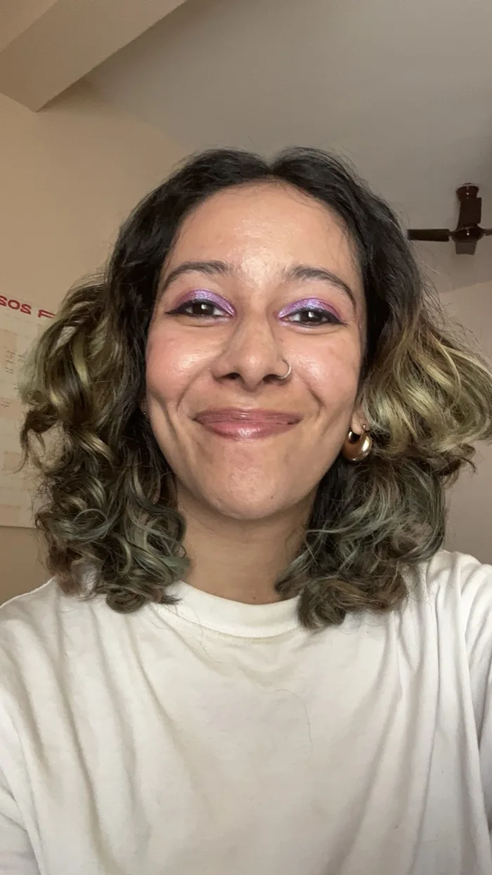 Saranyaa Ramesh, smiling, with curly shoulder-length hair, lavender eyeshadow and a white T-shirt.